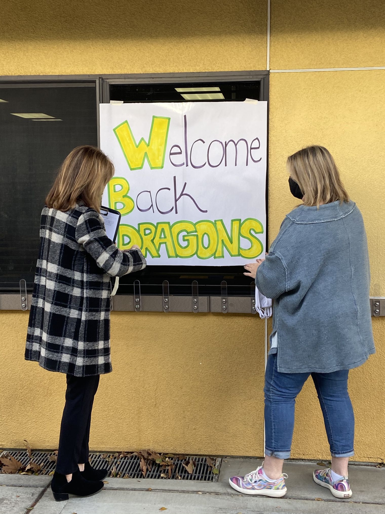 Two teachers hang up a welcome back sign for students