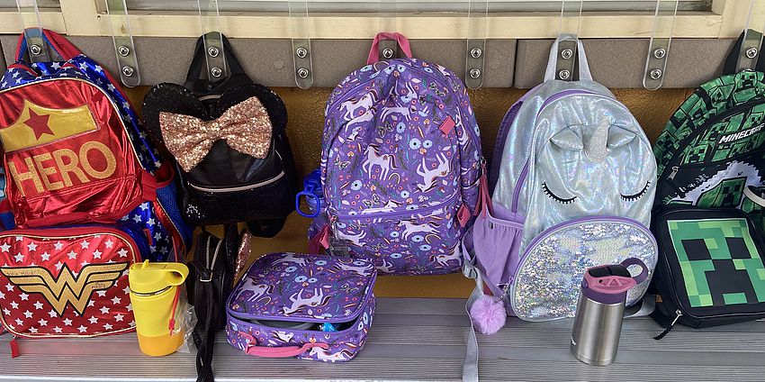 five child backpacks hanging from hooks outside classroom