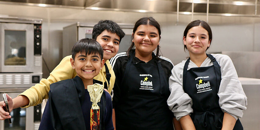 4 middle school students (2 boys and 2 girls) standing together and smiling as one boy holds a winners trophy