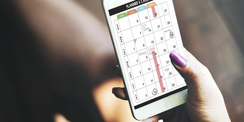 woman's hand holding a mobile device that shows a weekly planner