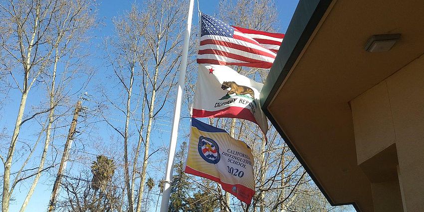 Three flags on a flag pole over Castlemont Elementary School
