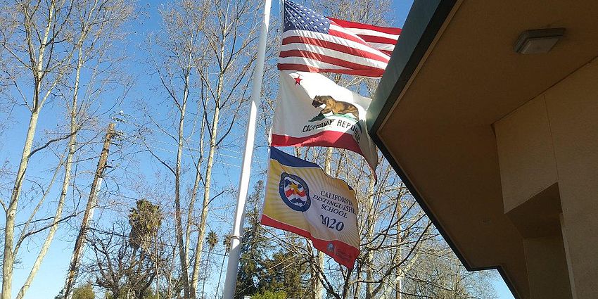 Three flags on a flag pole over Castlemont Elementary School