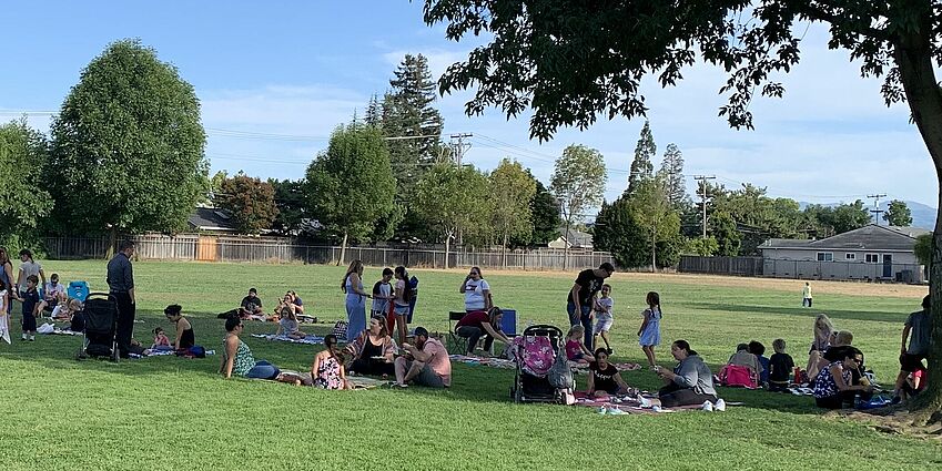 adults and children under a tree on picnic blankets