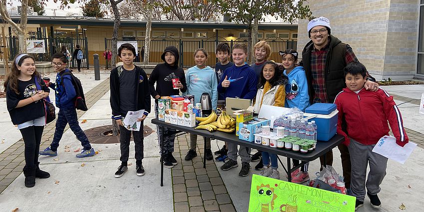 Castlemont fifth graders selling coffee, hot chocolate, and breakfast food at a table in front of the school.