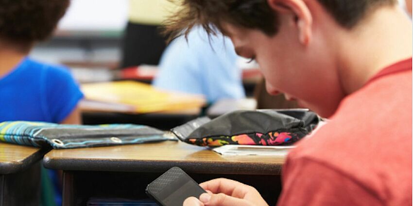 boy at desk sneaking cell phone use during class