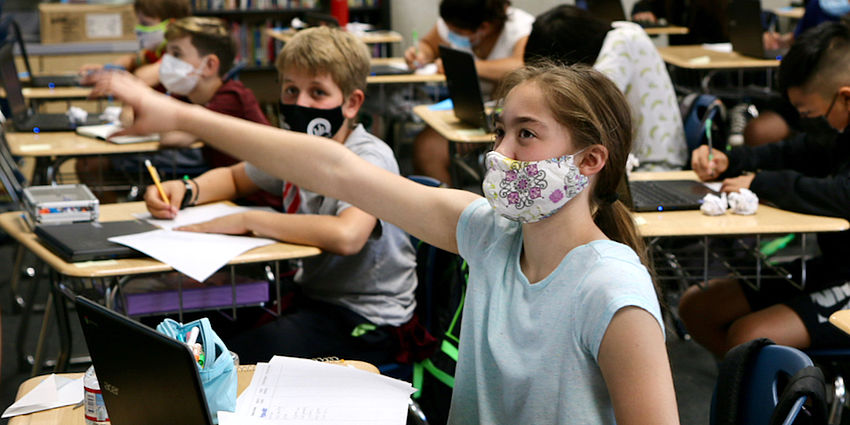 masked middle school girl raising hand in class