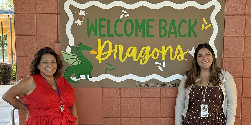 Two women standing front of a welcome back banner