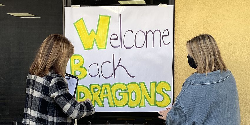 Two teachers hang up a welcome back sign for students