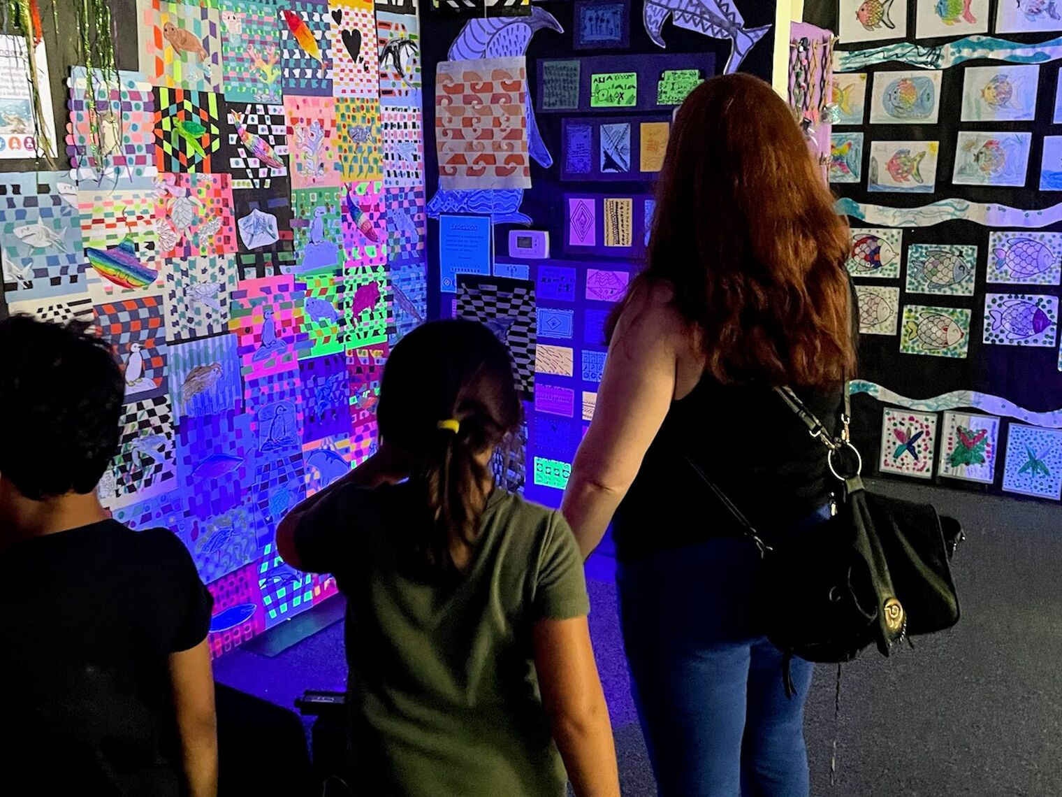 two children and their mom look at a colorful and glowing display of geometric artwork