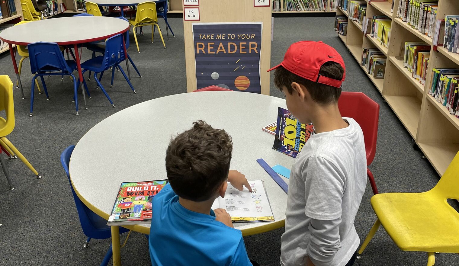 two boys in library in front of a sign that says Take Me To Your Reader