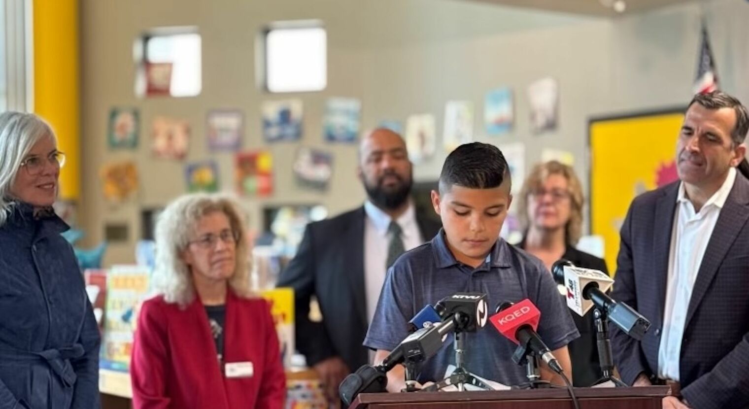 young boy at podium as several adults look on and listen