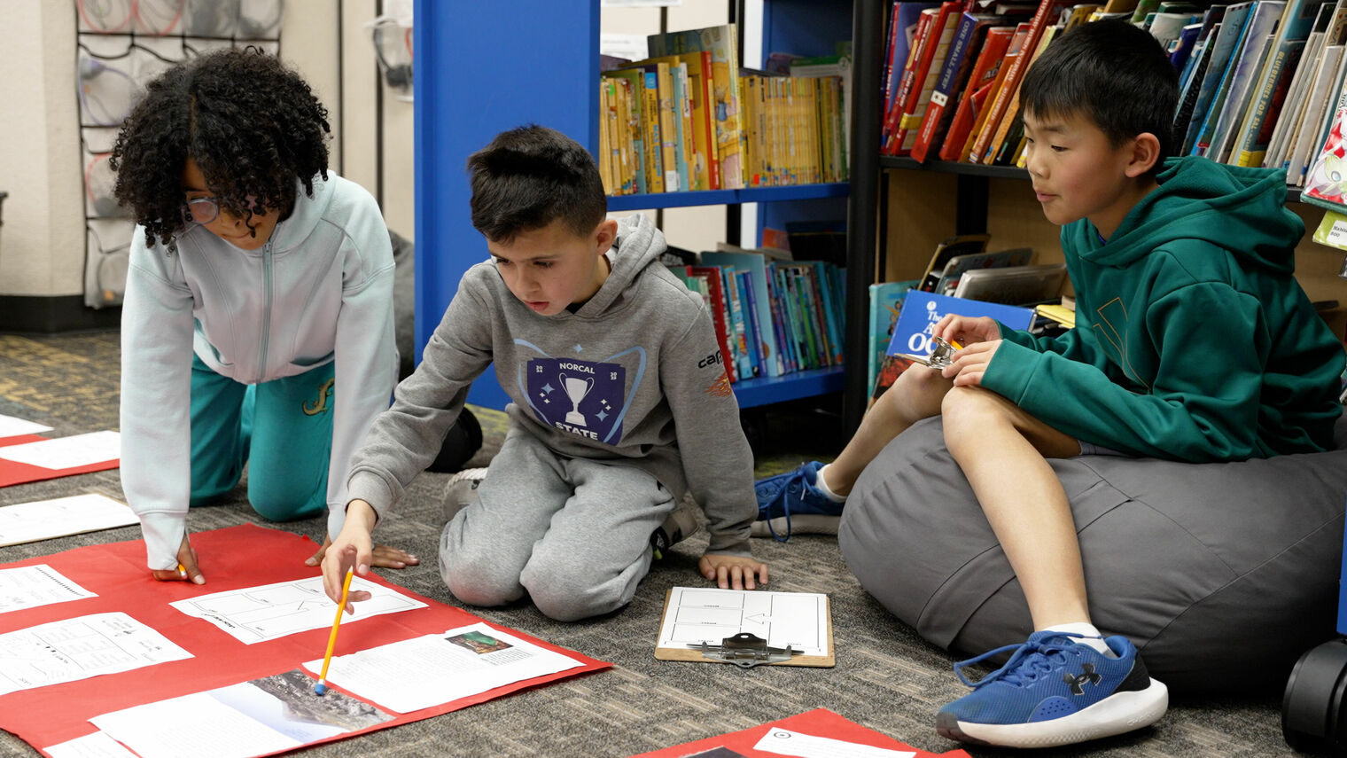 one girl and two boys sit on floor discussing the documents laying before them